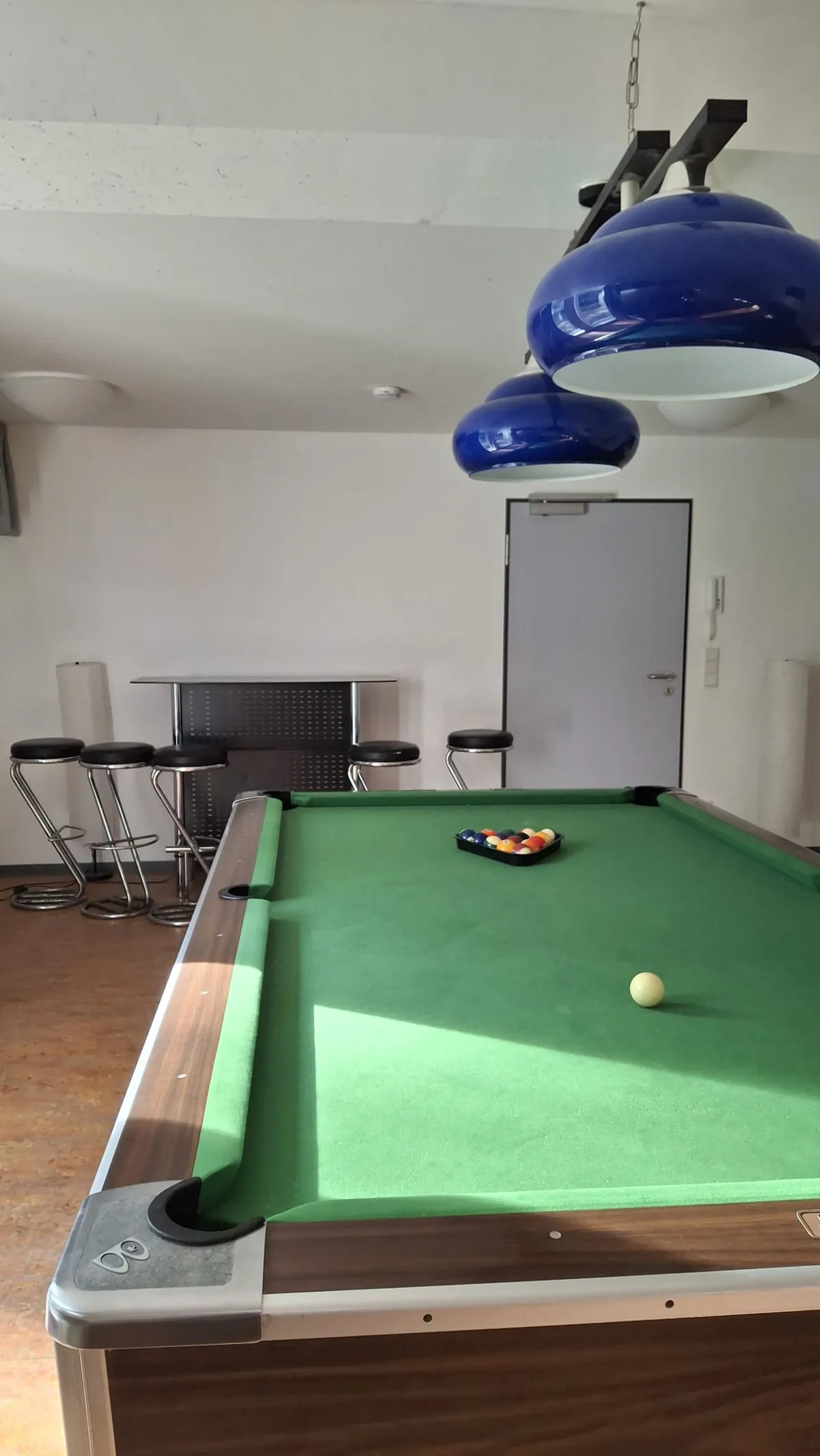 Billardtisch, dahinter Barhocker und Stehtisch