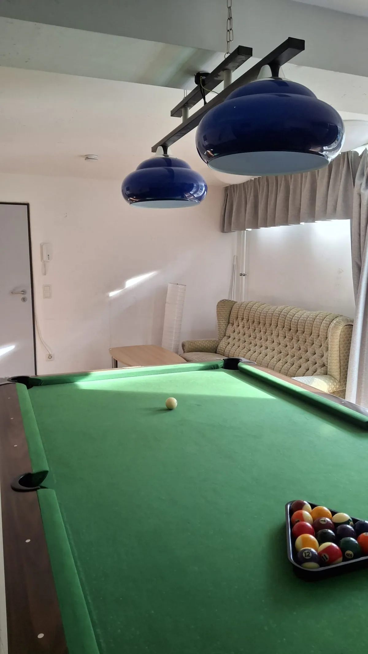 Billardtisch mit aufgebauten Kugeln und Sofa am Fenster